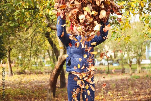 Defocus autumn people. Teen girl raising hand and throwing leaves. Many flying orange  yellow  green dry leaves. Joy autumn. Out of focus