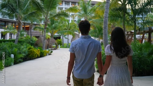 Young couple holding hands walking at all inclusive resort hotel in Caribbean. Tropical plans and luxury accommodations. Outside view. photo