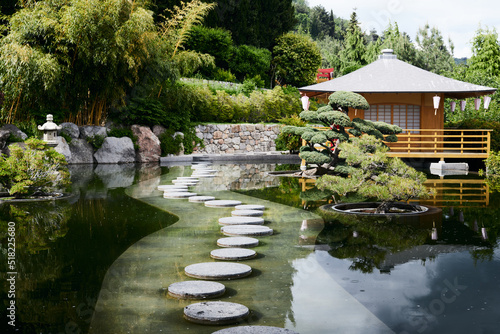 Japanese style house near the forest. A path of round stones across a pond in a Japanese garden. Front view.