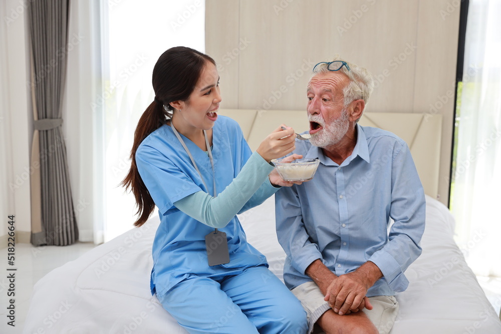 Obraz premium Happy caregiver feeding senior old man having cancer on bed with rice porridge soup for breakfast at retirement house. Asian smiling nurse taking good help care and support of elder patient at home.