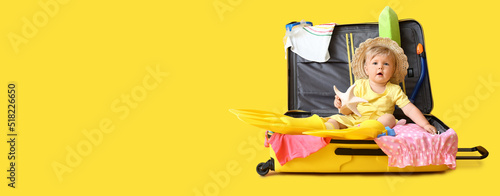 Cute baby girl sitting in suitcase on yellow background with space for text