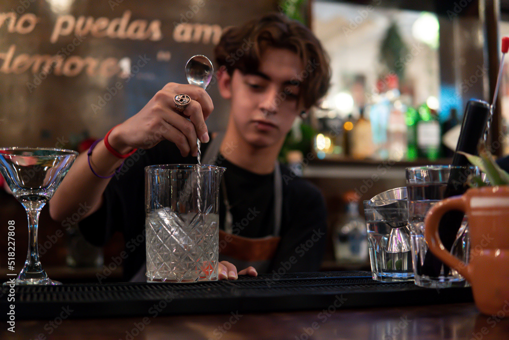 Concentrated young bartender preparing a glass with ice and drink for a client.