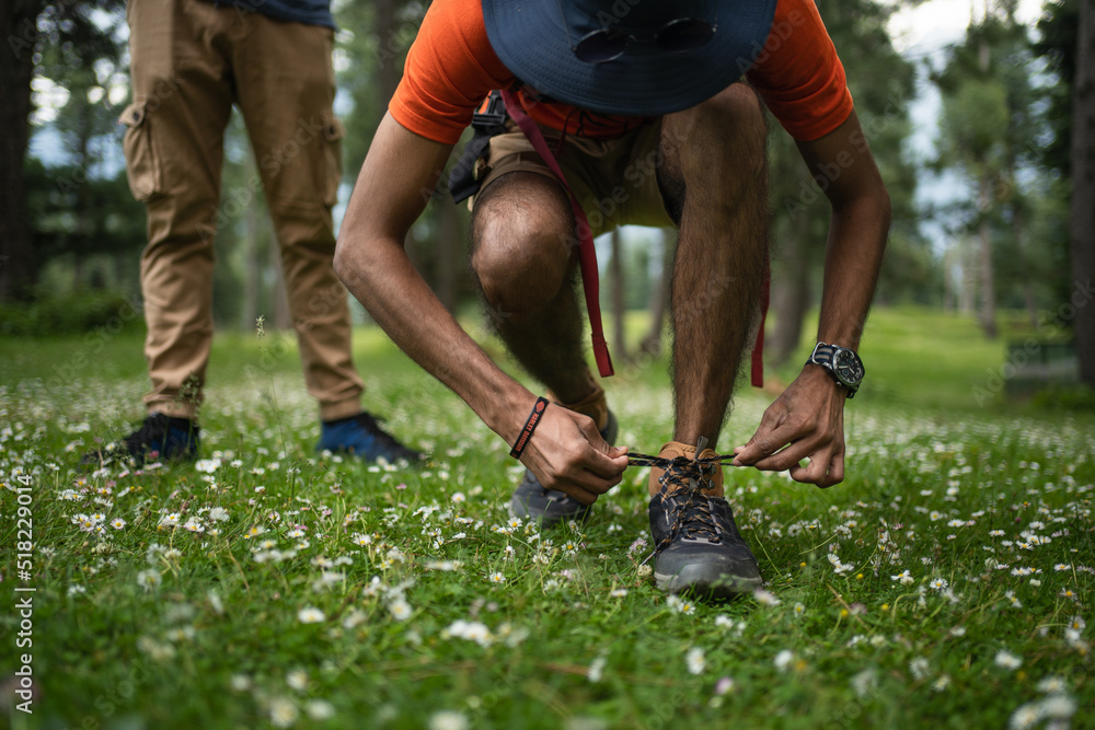 Man hiker with backpack stands on the Greenery and ties her shoe in Baisaran Valley, Pahalgam, Jaamu and Kashmir, India. Man hiker with backpack stands on the Greenery and ties her shoe in Baisaran Valley, Pahalgam, Jaamu and Kashmir, India.