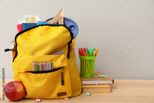 Photography School backpack with stationery and apple on table against grey background