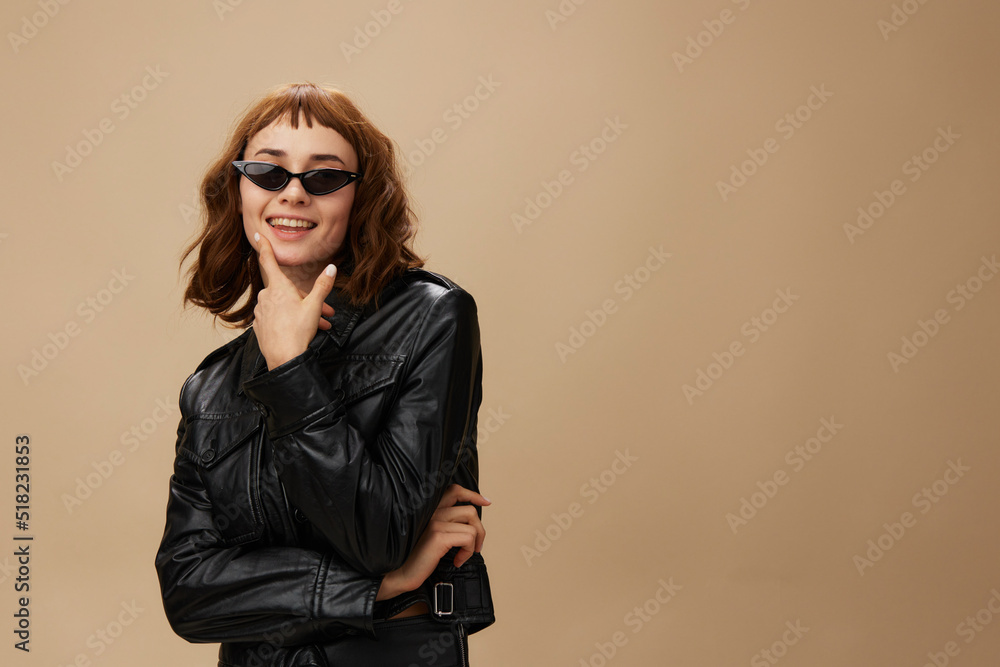 Funny adorable stylish pretty redhead lady in leather jacket sunglasses posing isolated on pastel beige studio background. Copy space Banner Offer. Over black concept. Fashion Cinema. Seasonal Sale Funny adorable stylish pretty redhead lady in leather jacket sunglasses posing isolated on pastel beige studio background. Copy space Banner Offer. Over black concept. Fashion Cinema. Seasonal Sale