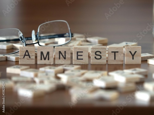 amnesty word or concept represented by wooden letter tiles on a wooden table with glasses and a book photo