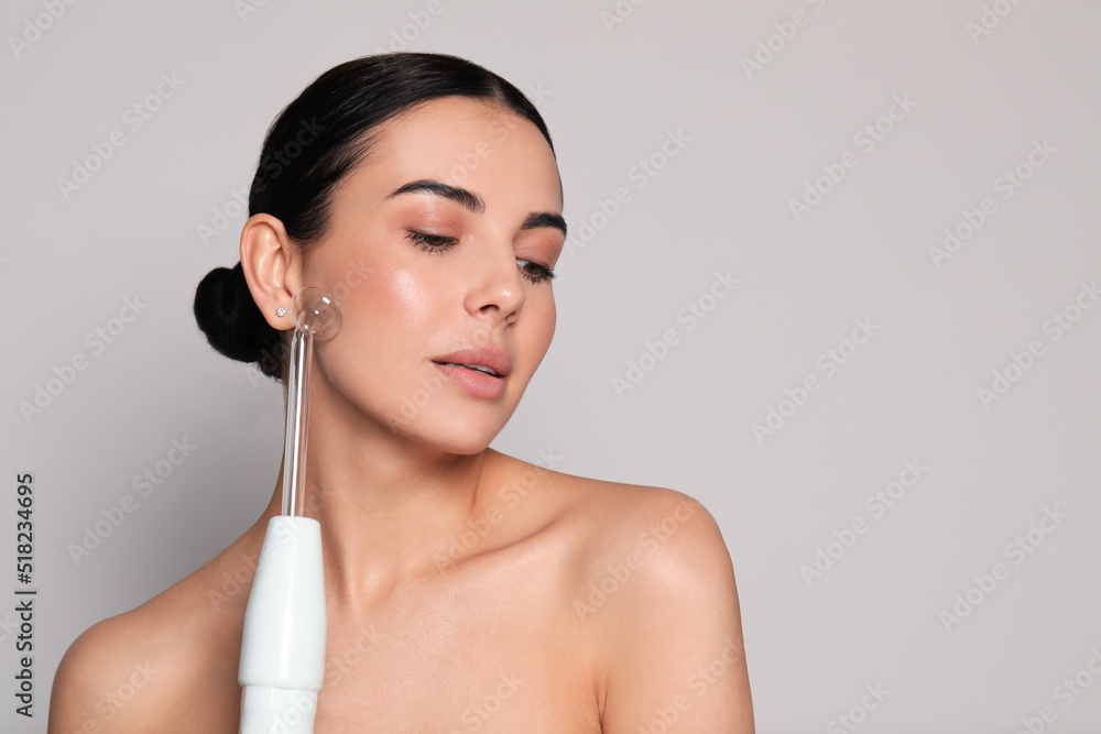 Woman using high frequency darsonval device on grey background. Space for text Woman using high frequency darsonval device on grey background. Space for text