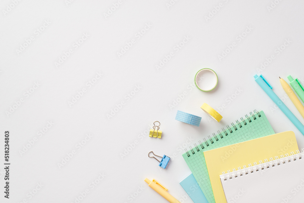School supplies concept. Top view photo of stationery stack of notepads pens binder clips and adhesive tape on isolated white background with copyspace School supplies concept. Top view photo of stationery stack of notepads pens binder clips and adhesive tape on isolated white background with copyspace