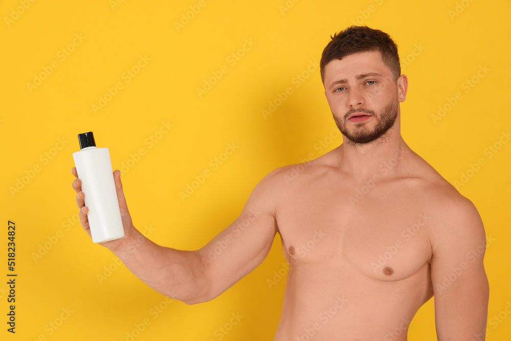 Fototapeta premium Shirtless young man holding bottle of shampoo on orange background