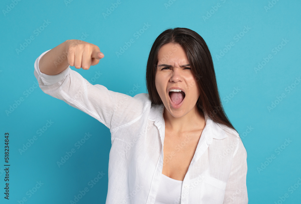 Fototapeta premium Aggressive young woman pointing on turquoise background