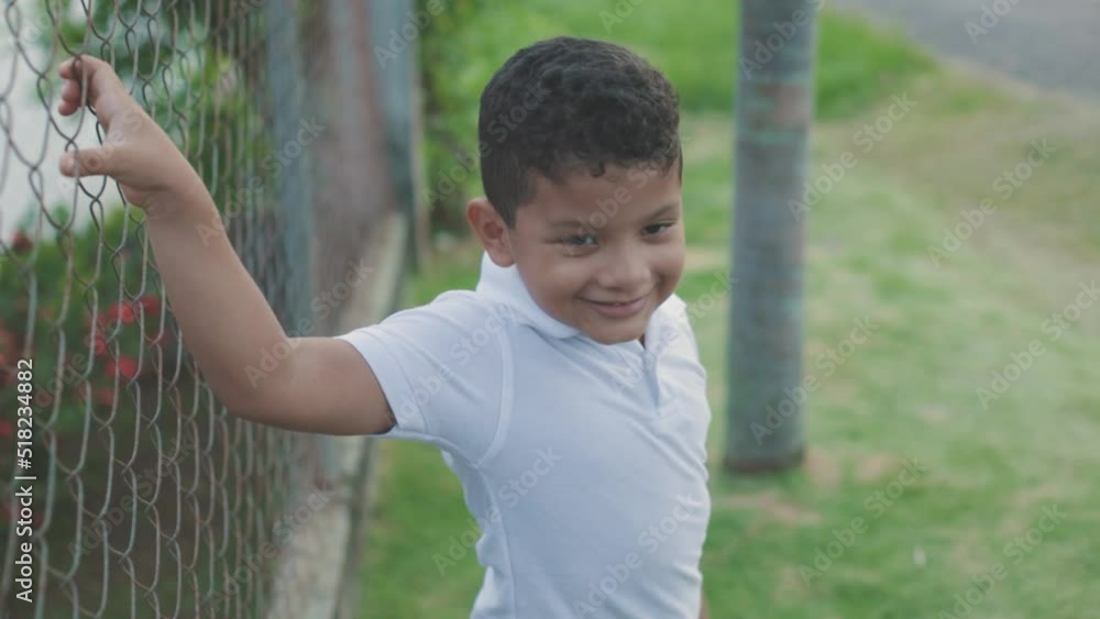 latino boy with white sweater, holding on to the cyclone wire while smiling, medium shot