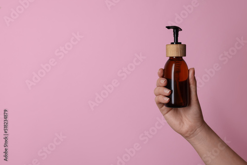 Woman holding bottle of cosmetic product on pink background, closeup. Space for text