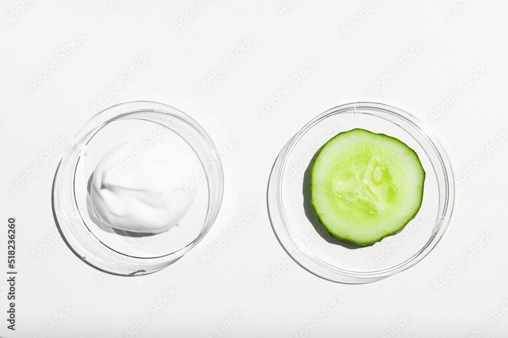 A sample of white cream, body lotion with a piece of green fresh cucumber on a white background with bright light. Moisturizing and nourishing the skin. A sample of white cream, body lotion with a piece of green fresh cucumber on a white background with bright light. Moisturizing and nourishing the skin.