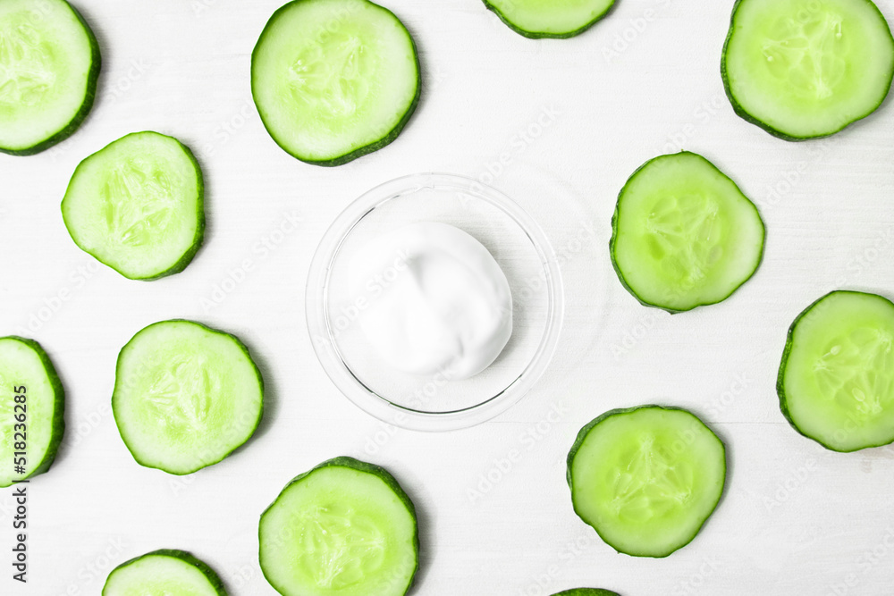Body cream sample with pieces of raw fresh green cucumber on a white wooden table. A hydrating, nourishing body treatment. Body cream sample with pieces of raw fresh green cucumber on a white wooden table. A hydrating, nourishing body treatment.