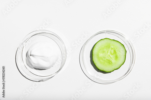A sample of white cream, body lotion with a piece of green fresh cucumber on a white background with bright light. Moisturizing and nourishing the skin.
