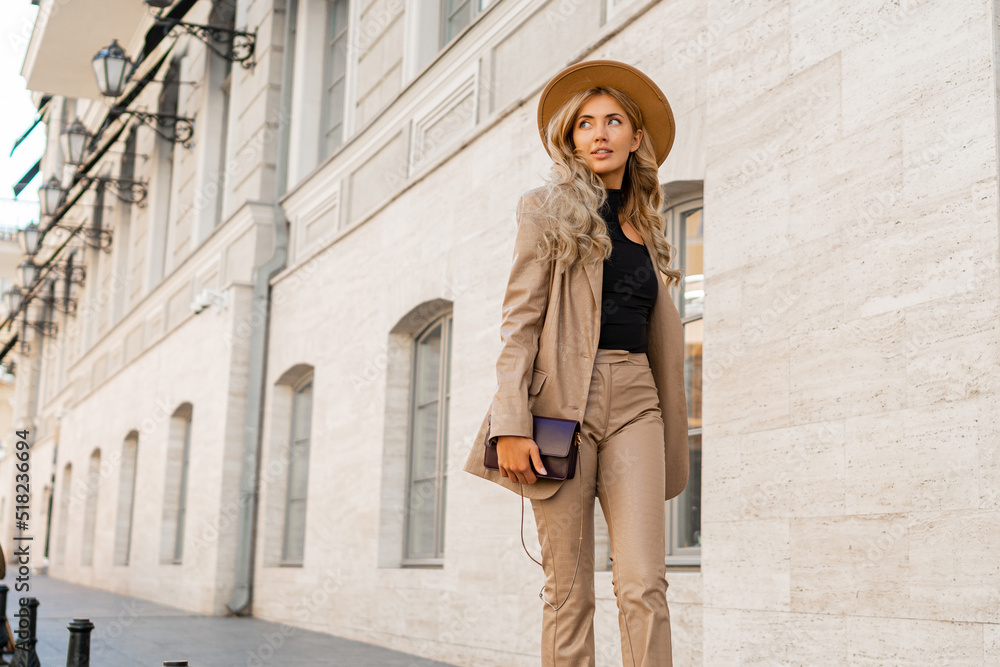 Fashion photo of gorgeous beutiful blond model posing in trendy leather  jacket and pants outdoor. Wearing beige hat.