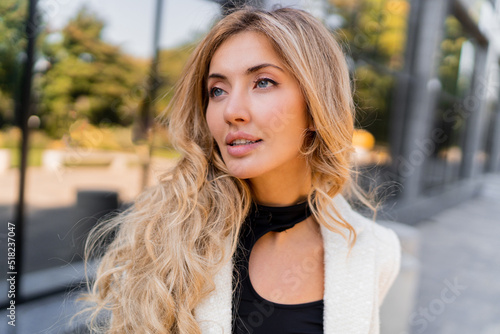 Fototapeta Close up portrait of stylish  pretty blond woman with perfect wavy hairs and full lips in casual jacket posing over modern stree