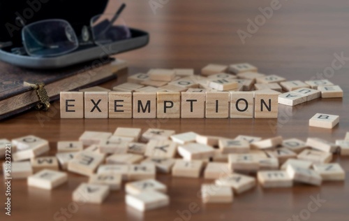 exemption word or concept represented by wooden letter tiles on a wooden table with glasses and a book photo
