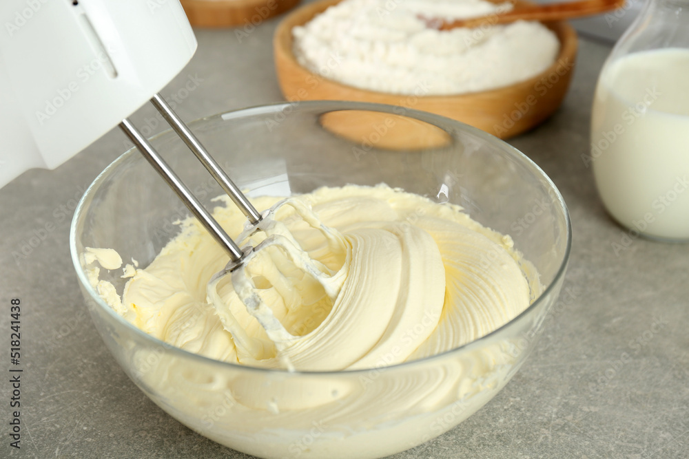 Whipping white cream in glass bowl with mixer on light grey table, closeup Whipping white cream in glass bowl with mixer on light grey table, closeup