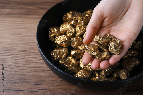 Woman with gold nuggets at wooden table, closeup
