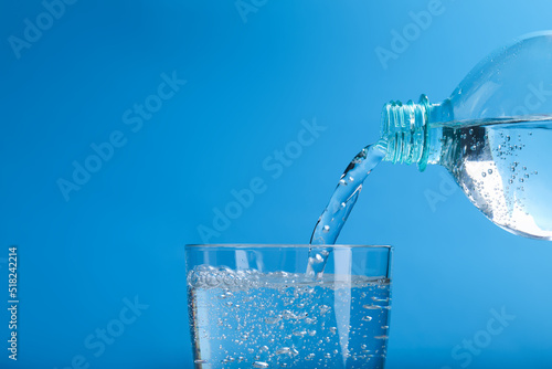Pouring soda water from bottle into glass on light blue background, closeup. Space for text
