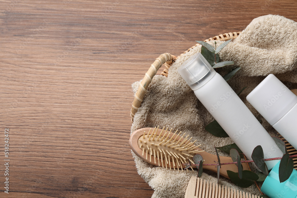 Φωτογραφία Dry shampoo sprays, towel and hairbrushes with eucalyptus branch in basket on wooden table, top view