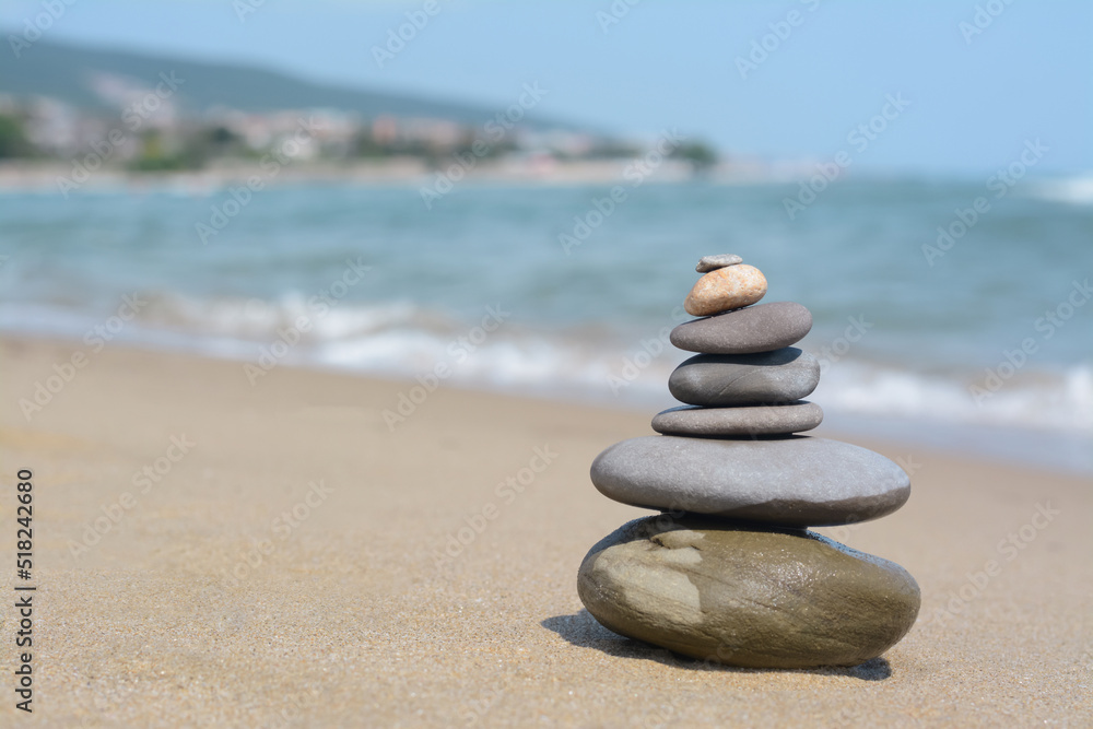 Fototapeta premium Stack of stones on sandy beach near sea, space for text