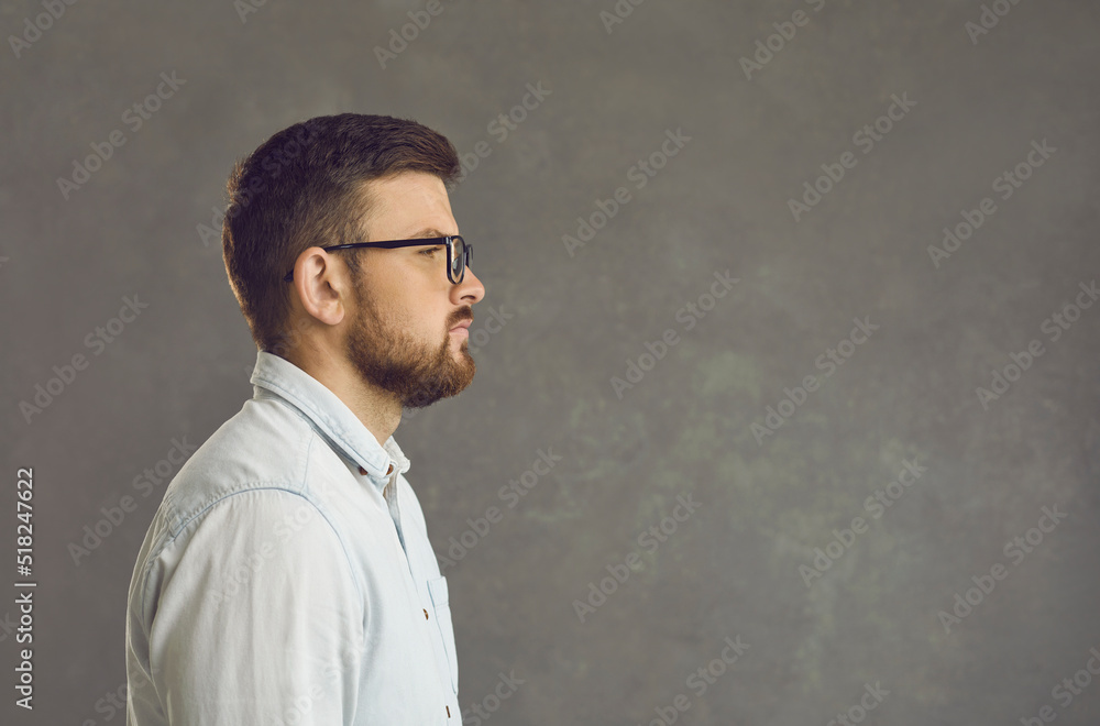 Side view studio portrait of young serious confident concentrated business man executive manager or freelancer in elegant shirt and rimmed eyeglasses looking at gray copy space background