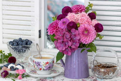 Tischdekoration mit Blumenstrauß in Pink, Tasse Kaffee und Heidelbeeren