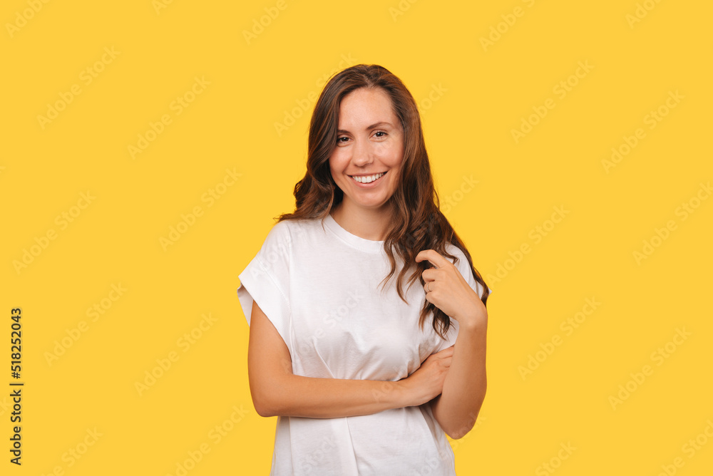 Obraz premium A young female is smiling and looking at the camera is posing near a yellow wall .