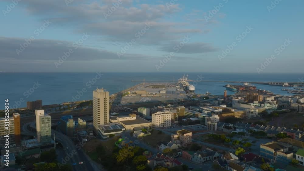 Forwards fly above coastal town at golden hour. Oversea harbour and large ships. Port Elisabeth, South Africa Forwards fly above coastal town at golden hour. Oversea harbour and large ships. Port Elisabeth, South Africa