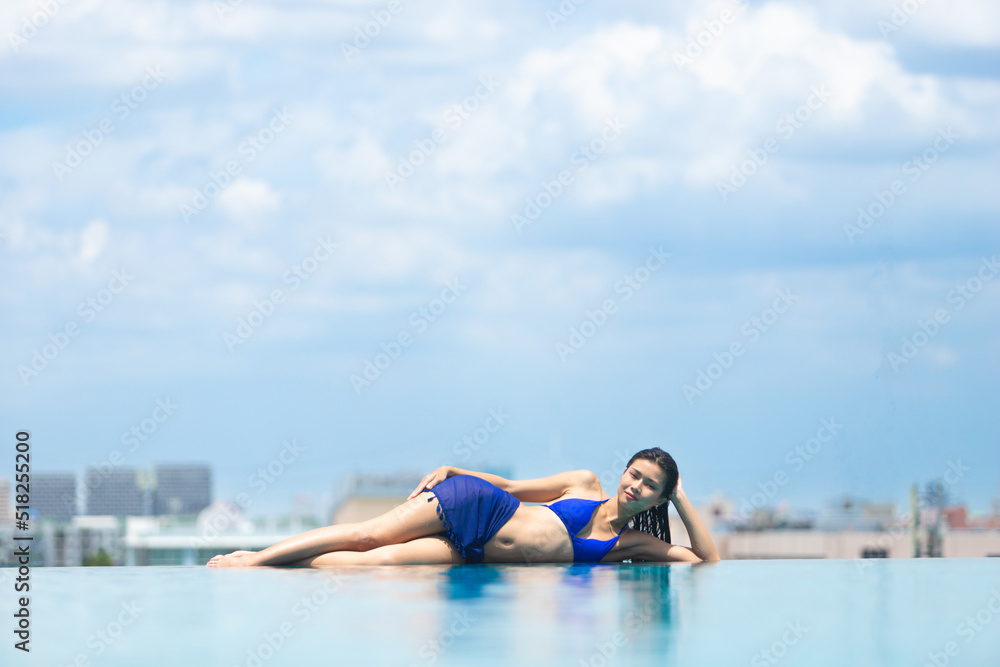 Young 20s Asian Woman lie sleep along swimming pool horizon edge with blue sky city view