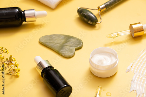 Serum and moisturizing cosmetic cream with facial massager on colored background