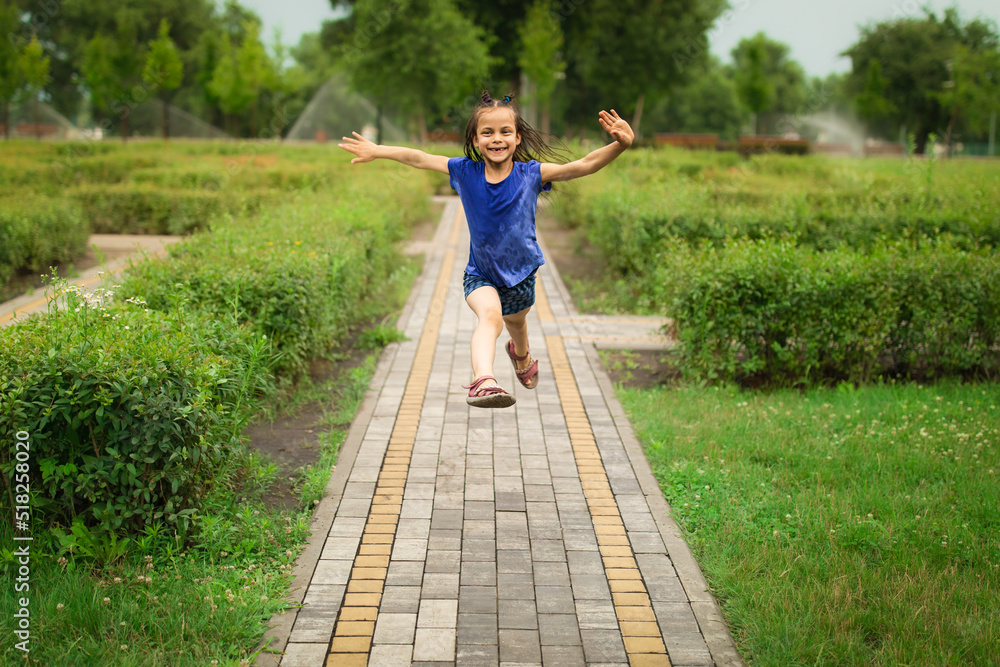 Little adorable girl jumping in beautiful green park in summer