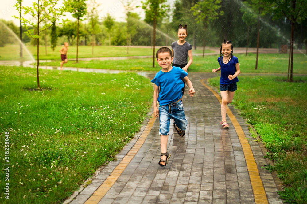 Children running in park with watering devices and having fun being under water in summer