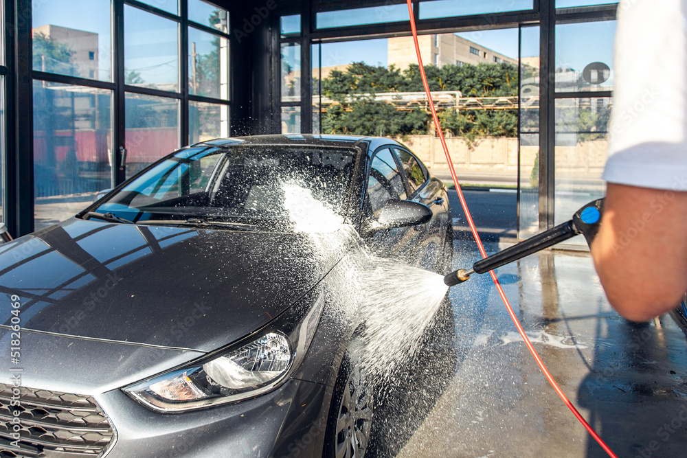 Self-service car wash. A man waters his car with foam from a pressurized hose