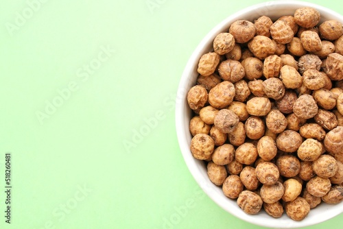 Chufa, tigernut, earth almond on ceramic bowl on green background with copy space for text. Healthy organic food concept. Tiger nut for flour, milk, traditional typical drink horchata Valencia Spain