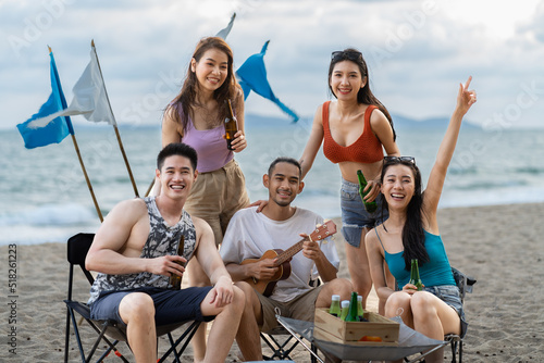 Group of Asian young man and woman having party on the beach at night. Attractive friends traveler sing and dance while camping at seaside enjoy holiday vacation trip in tropical sea island together.