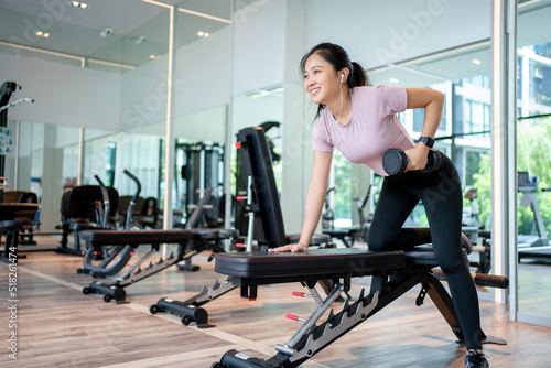 Smiling slim fit sportswoman doing exercises with weights over fitness bench at the gym