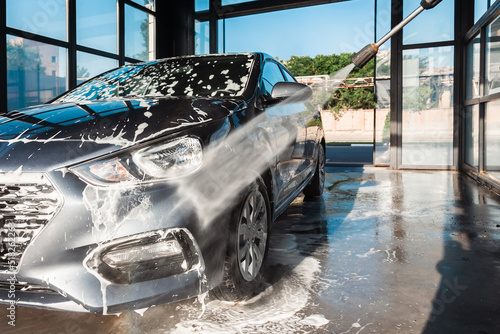 Self-service car wash. A man washes off the foam from his car with water from a pressurized hose at a self-service car wash