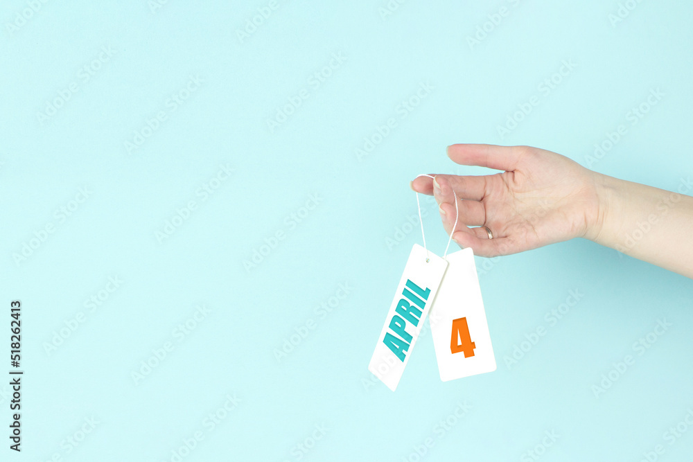 April 4th. Day 4 of month, Calendar date. Hand hold price tag with calendar date on blue background. Spring month, day of the year concept. April 4th. Day 4 of month, Calendar date. Hand hold price tag with calendar date on blue background. Spring month, day of the year concept.