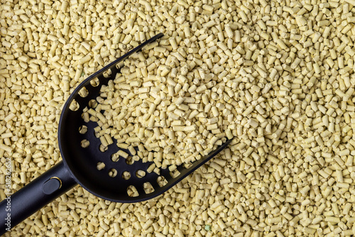 Hygienic natural clumping cat litter with black scoop or spatula for cleaning. Texture of vegetable fiber granules. Yellow corn tofu close up.