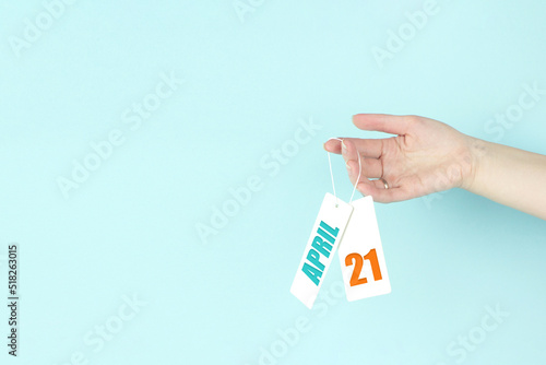 April 21st . Day 21 of month, Calendar date. Hand hold price tag with calendar date on blue background. Spring month, day of the year concept.