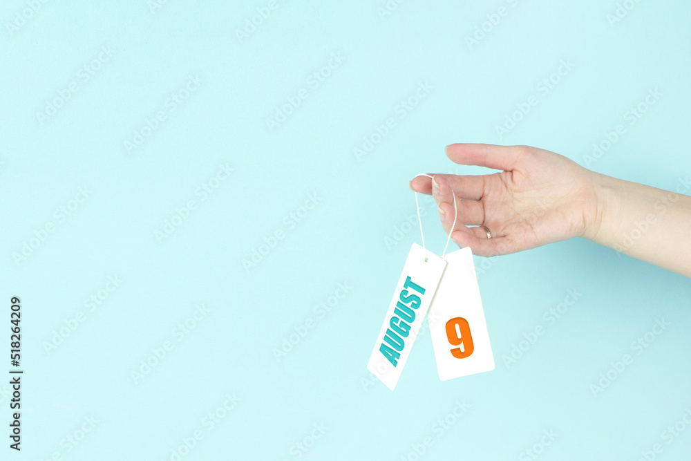 August 9th. Day 9 of month, Calendar date. Hand hold price tag with calendar date on blue background. Summer month, day of the year concept. August 9th. Day 9 of month, Calendar date. Hand hold price tag with calendar date on blue background. Summer month, day of the year concept.