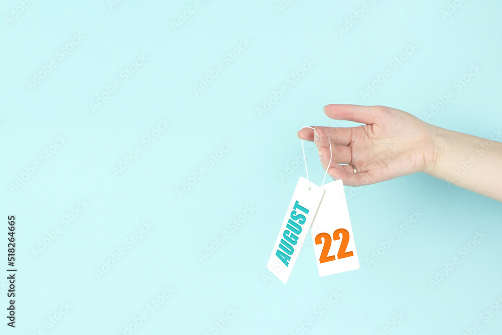 August 22nd. Day 22 of month, Calendar date. Hand hold price tag with calendar date on blue background. Summer month, day of the year concept. August 22nd. Day 22 of month, Calendar date. Hand hold price tag with calendar date on blue background. Summer month, day of the year concept.