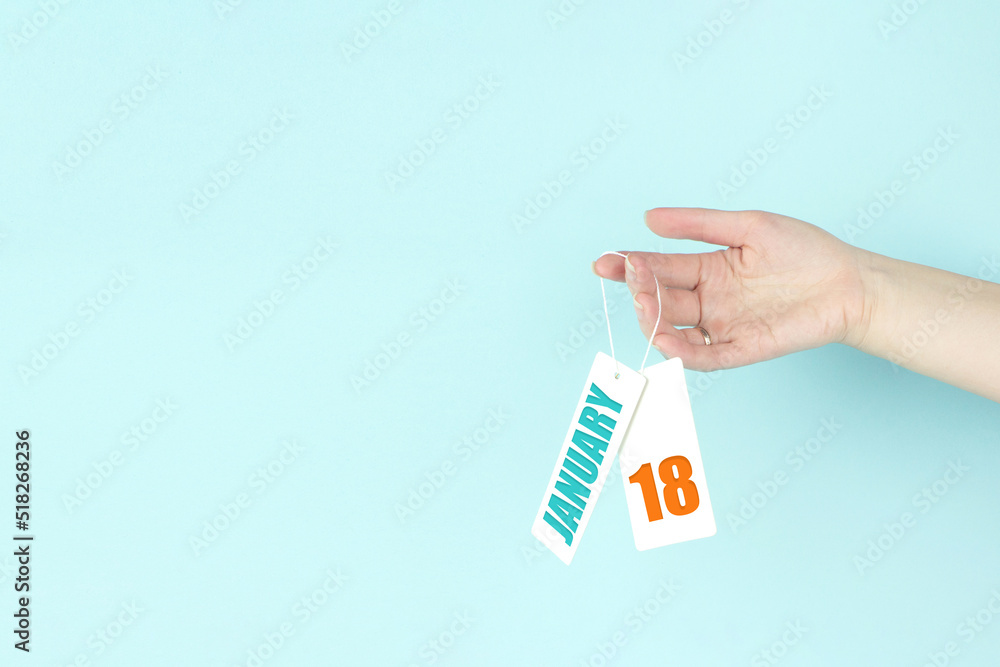 January 18th. Day 18 of month, Calendar date. Hand hold price tag with calendar date on blue background. Winter month, day of the year concept. January 18th. Day 18 of month, Calendar date. Hand hold price tag with calendar date on blue background. Winter month, day of the year concept.