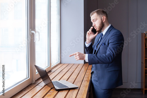Businessman working in office. Guy using smart phone and pointing at laptop