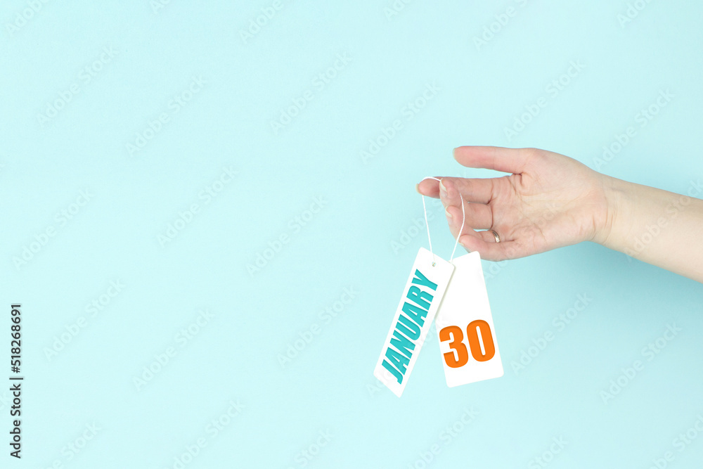 January 30th. Day 30 of month, Calendar date. Hand hold price tag with calendar date on blue background. Winter month, day of the year concept. January 30th. Day 30 of month, Calendar date. Hand hold price tag with calendar date on blue background. Winter month, day of the year concept.