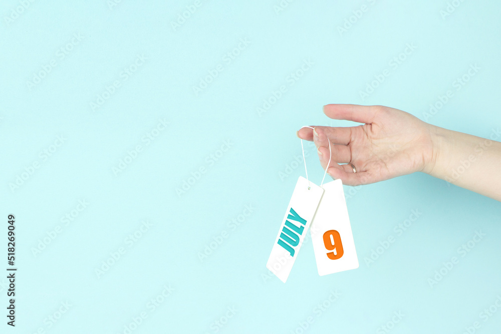 July 9th. Day 9 of month, Calendar date. Hand hold price tag with calendar date on blue background. Summer month, day of the year concept. July 9th. Day 9 of month, Calendar date. Hand hold price tag with calendar date on blue background. Summer month, day of the year concept.