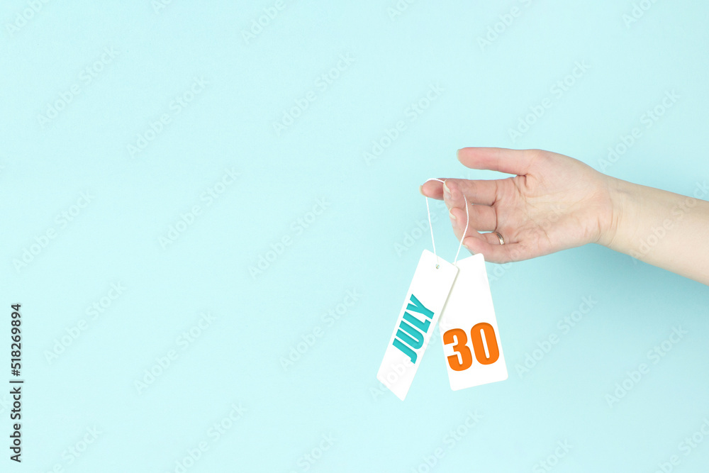 July 30th. Day 30 of month, Calendar date. Hand hold price tag with calendar date on blue background. Summer month, day of the year concept. July 30th. Day 30 of month, Calendar date. Hand hold price tag with calendar date on blue background. Summer month, day of the year concept.